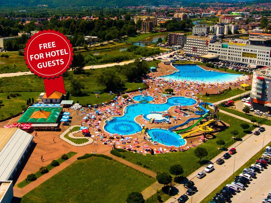 Hotel Hills Sarajevo Congress & Thermal Spa Resort Ilidža Екстериор снимка The photo shows an aerial view of a large swimming pool area, likely part of a hotel or resort. There are several pools of different shapes and sizes, including one that resembles a Mickey Mouse shape. The area is filled with numerous sun loungers an